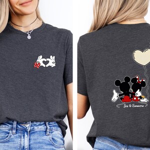 May include: Dark grey t-shirt with a Mickey Mouse and Minnie Mouse design. The front shows hands forming a heart, and the back displays the couple with a heart-shaped balloon. The names "Joe & Samantha" are written below.