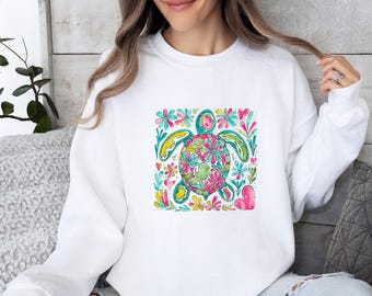 May include: A white long-sleeve sweatshirt featuring a central graphic illustration of a sea turtle. The turtle shell and surrounding area are decorated with vibrant, colorful floral patterns in shades of pink, teal, yellow, and green.