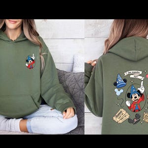 Op de afbeelding: Olijfgroene hoodie met een Mickey Mouse-ontwerp. De voorkant heeft een kleine Mickey Mouse-afbeelding, terwijl de achterkant een groter ontwerp heeft met de tekst "Some imagination, Huh?" en andere gerelateerde illustraties. De hoodie heeft een voorzak.