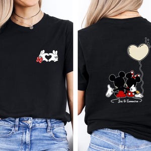May include: Black t-shirt with a heart made of white cartoon hands and a red bow. The back of the shirt shows Mickey and Minnie Mouse with a heart-shaped balloon and the names "Joe & Samantha".