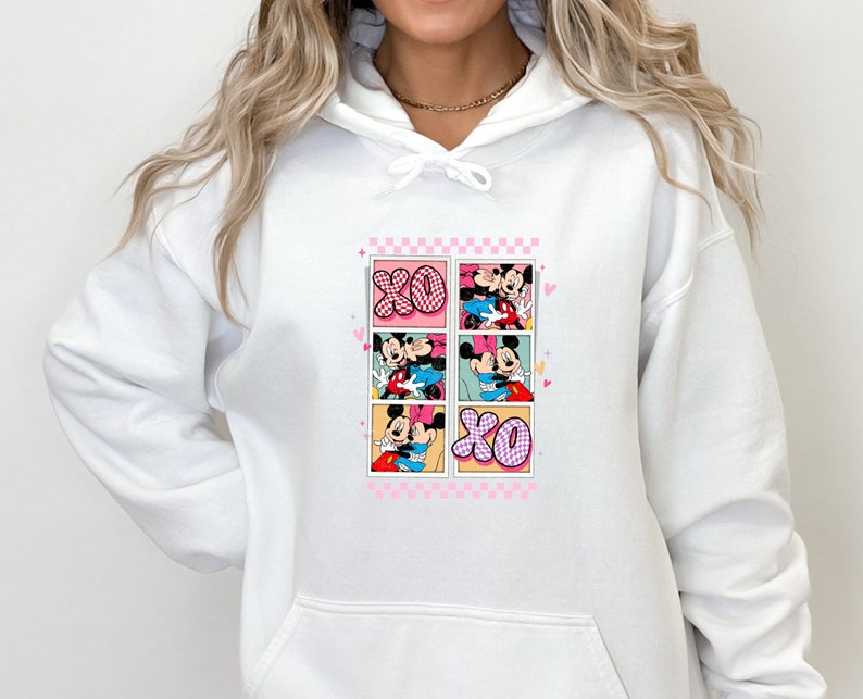 May include: White hoodie featuring a colorful graphic of Mickey and Minnie Mouse in various romantic poses. The design includes the letters "XO" and a pink checkered border, perfect for Valentine's Day or Disney fans.