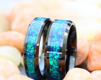 May include: Two black rings with a vibrant blue and green opal inlay. The rings are set against a backdrop of small, colorful stones, creating a striking contrast. The rings are a stylish accessory.