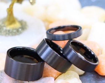 May include: Four black tungsten carbide rings stacked on top of each other. The rings have a brushed finish and are a popular choice for wedding bands.