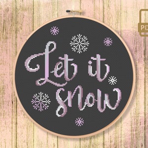 May include: A black and white cross-stitch pattern with the text "Let it snow" in a pink gradient. The pattern is surrounded by small snowflake designs.