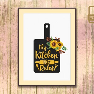 May include: Black and white cross stitch pattern of a chopping board with sunflowers and the text "My Kitchen My Rules".