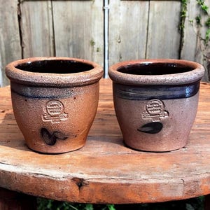 May include: Two brown stoneware crocks with blue glaze and a white label that reads "Howe's Patent Stoneware 1860".