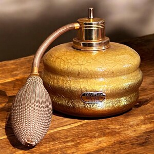 May include: A vintage gold-toned perfume bottle with a bulb atomizer. The bottle has a textured, crackled finish and a gold-colored metal top. The atomizer bulb is a woven mesh. The bottle has a label that reads "DeVilss".