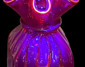 May include: A vibrant, purple glass vase with a ruffled rim and a unique, textured design. The rim is outlined with a thin orange border. The vase has a bulbous shape with vertical lines and orange accents.