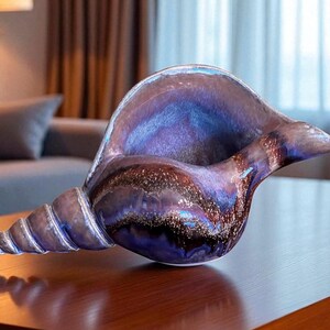 May include: A decorative, iridescent glass seashell sculpture. The art piece features a spiral base and a wide opening, with shades of blue, purple, and brown. The seashell is displayed on a wooden table.