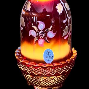 May include: A Fenton handpainted glass lamp with a dome-shaped shade featuring a red and orange gradient, decorated with painted floral and leaf motifs. The base has a textured, diamond-patterned red glass design with a scalloped rim edge.