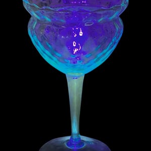 May include: A blue glass goblet with a wide, scalloped rim and a textured, bulbous body. The goblet is illuminated from below, casting a purple glow.
