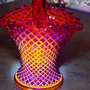 May include: A red and yellow glass basket with a diamond pattern. The basket has a twisted handle and a scalloped rim.