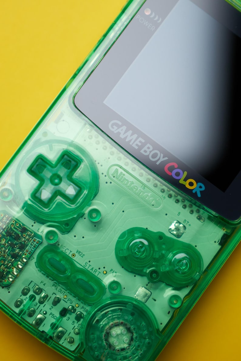 Op de afbeelding: Een draagbare Game Boy Color spelcomputer met een doorschijnende neongroene plastic behuizing. Het apparaat toont het Nintendo-logo en de tekst Game Boy Color op de schermrand, met zichtbare interne circuits, een richtingspad en diverse knoppen.