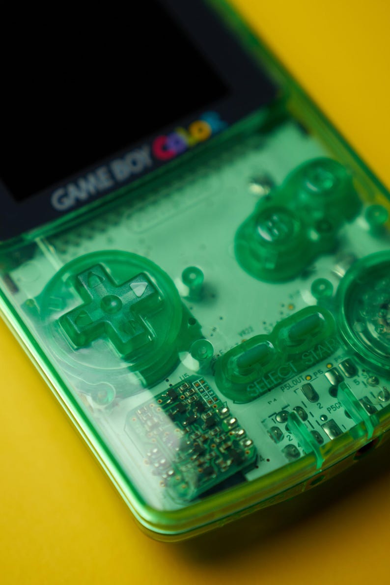 Op de afbeelding: Een doorschijnende limoengroene Game Boy Color handheld spelcomputer met een zichtbare interne printplaat, een richtingspad, A- en B-knoppen, en Select- en Start-knoppen. Het schermframe toont het Game Boy Color logo.