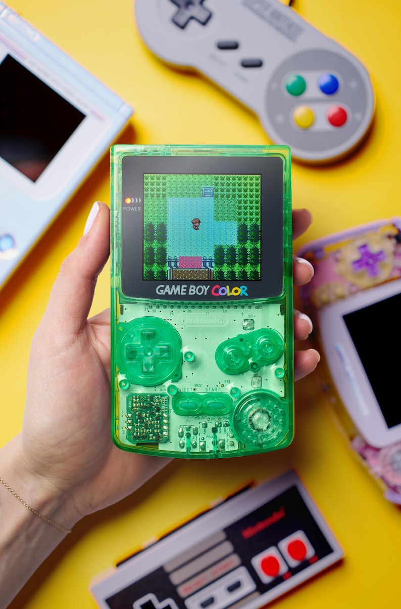 Op de afbeelding: Een limoengroene doorschijnende Game Boy Color handheld spelcomputer met een zichtbare interne printplaat, een richtingspad, twee actieknoppen en een scherm dat een gepixeld personage in een groene spelomgeving weergeeft.