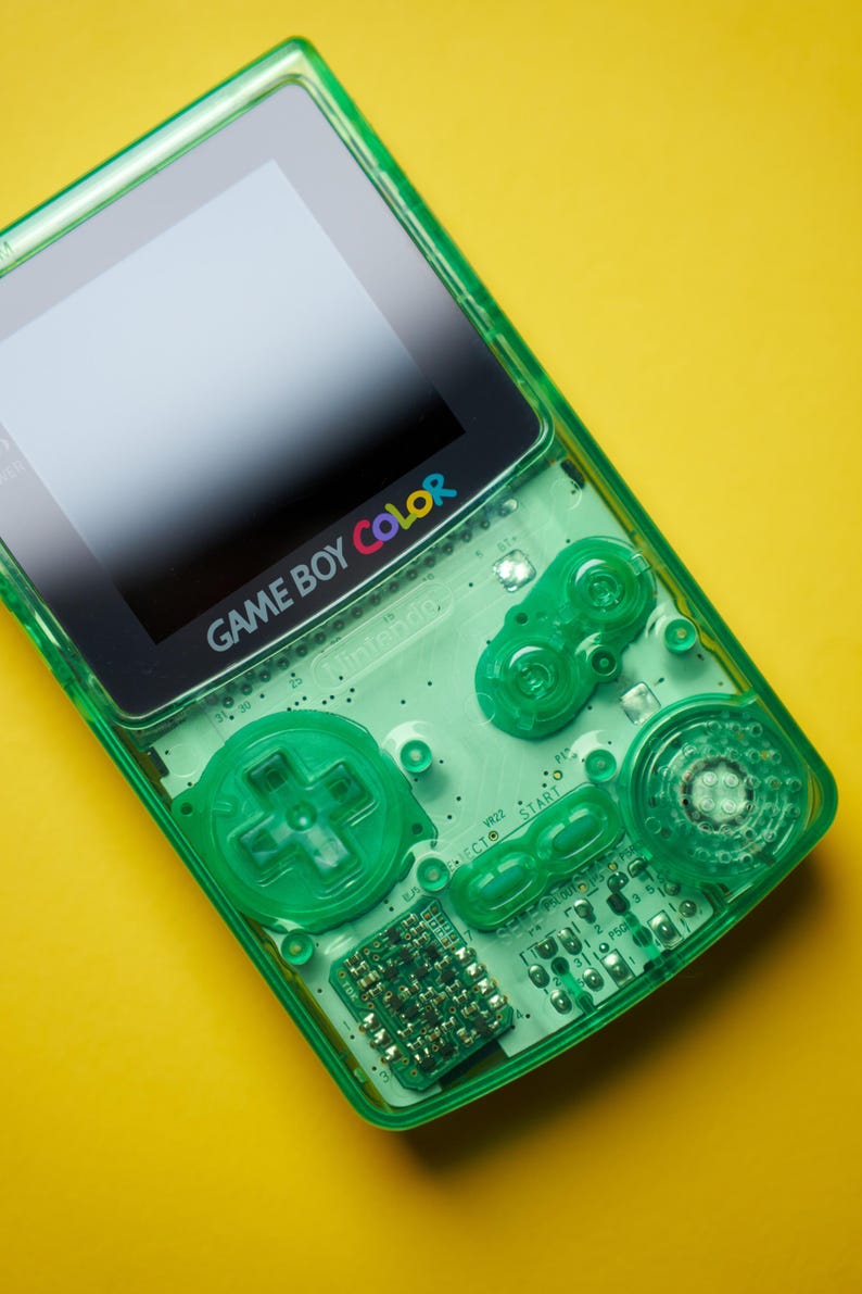 Op de afbeelding: Een doorschijnende limoengroene Game Boy Color handheld spelcomputer met een zichtbare interne printplaat, een richtingspad, A- en B-knoppen, en Start- en Select-knoppen. Het schermframe toont het Game Boy Color logo.