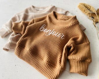 May include: A brown waffle knit sweater with long sleeves and a white embroidered "bonjour" on the front.