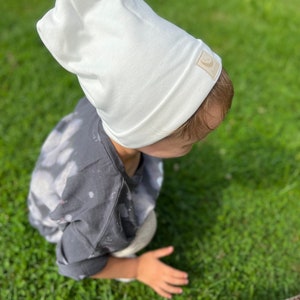May include: A white beanie with a small brown label on the side. The beanie is made of a soft, comfortable fabric and is perfect for keeping warm in the winter.