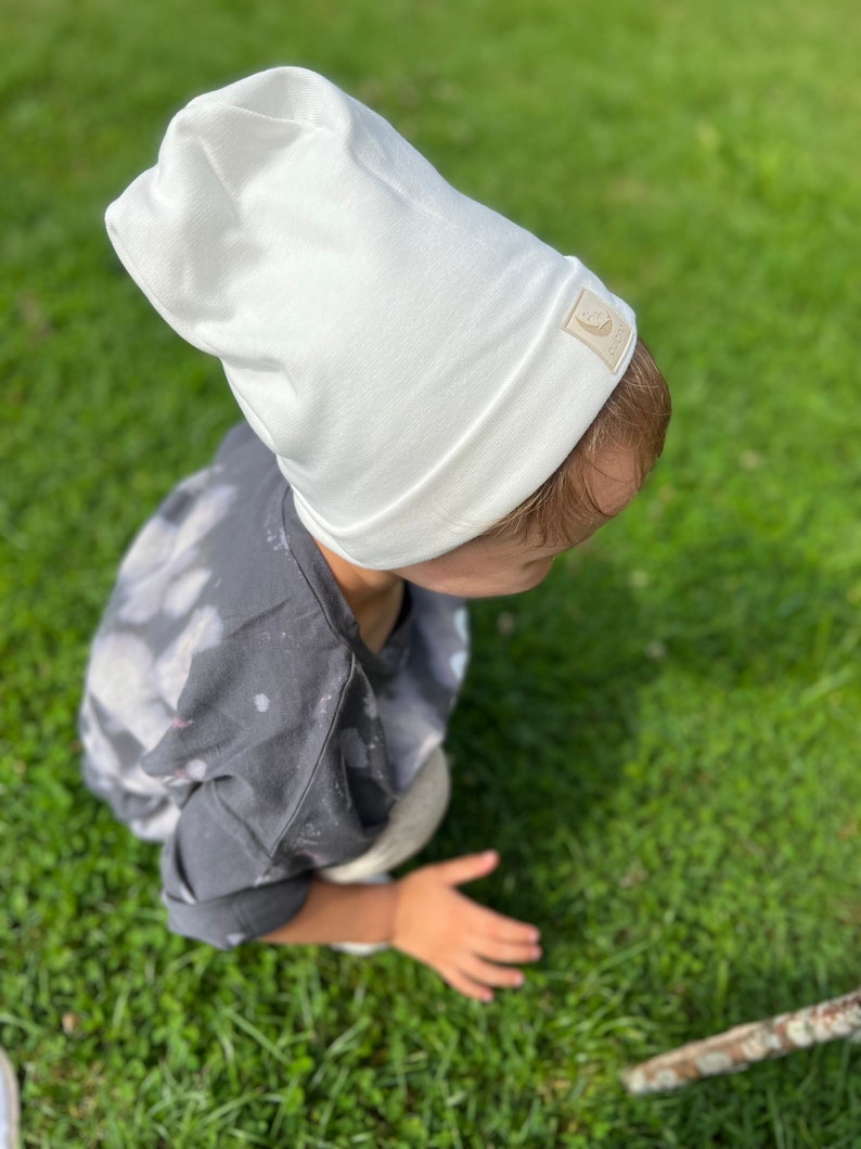 May include: A white beanie with a small brown label on the side. The beanie is made of a soft, comfortable fabric and is perfect for keeping warm in the winter.