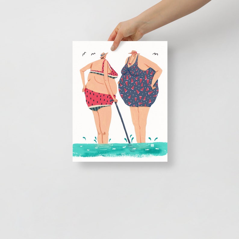 May include: Two women in swimsuits stand in the water. One woman is wearing a watermelon print swimsuit and the other is wearing a blue swimsuit with watermelon slices printed on it. They are both smiling and looking at each other.
