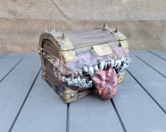May include: A wooden treasure chest with a monstrous mouth design. The chest is brown with gold accents and metal hardware. The mouth features sharp teeth and a red tongue, creating a fantasy or horror theme.