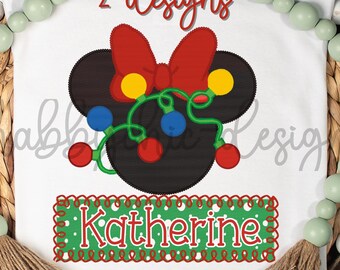 May include: A white t-shirt with a black and red Mickey Mouse head design. The Mickey Mouse head has a red bow and is decorated with a string of colorful Christmas lights. The text "2 designs" is at the top of the shirt. The text "Katherine" is on a green and red banner at the bottom of the shirt.
