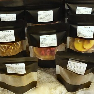 May include: Nine black zippered pouches with clear windows, each containing dried herbs and flowers. The pouches are labeled with names like "Balance", "Passion", "Samhain", and "Protection".