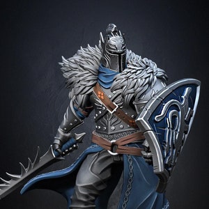 Op de afbeelding: Een miniatuurfiguur van een ridder met een zilveren helm met een blauwe cape en een bontkraag, die een zwaard en schild vasthoudt. De ridder staat op een stenen basis.