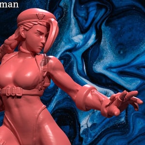 May include: A pink figurine of a female character in a dynamic pose, wearing a leotard, boots, and gloves. The figure has a long braid and a beret. The text "patreon.com/irnkman" is visible in the upper left corner. The figurine is from "Irnkman's Minis".