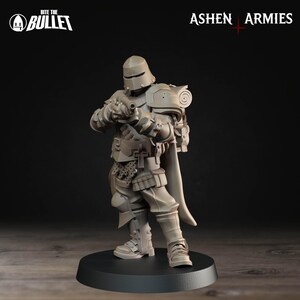 Op de afbeelding: Grijze miniatuurfiguur van een soldaat in volledige bepantsering, met een geweer. De figuur heeft een helm, schouderbeschermers en een cape. De basis is zwart en de figuur staat erop. De teksten "Bite the Bullet" en "Ashen Armies" zijn zichtbaar.