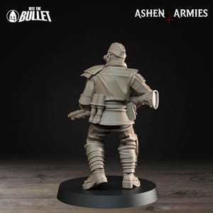 Op de afbeelding: Miniatuurbeeldje van een soldaat in een beige uniform, gezien van achteren. De figuur staat op een zwarte basis. Het uniform omvat een hoed, schouderstukken en meerdere zakken. De tekst "Bite the Bullet" en "Ashen Armies" zijn zichtbaar.