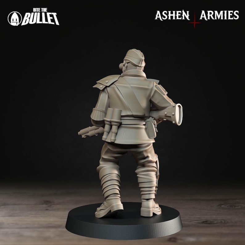 Op de afbeelding: Miniatuurbeeldje van een soldaat in een beige uniform, gezien van achteren. De figuur staat op een zwarte basis. Het uniform omvat een hoed, schouderstukken en meerdere zakken. De tekst "Bite the Bullet" en "Ashen Armies" zijn zichtbaar.