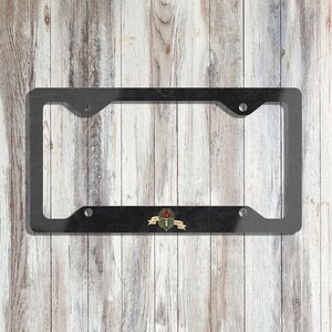 May include: Black metal license plate frame with a decorative design featuring a ribcage with a red rose and the text "Til Death Do Us Part".