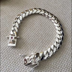 May include: A silver curb chain bracelet with a small red stone on the clasp.