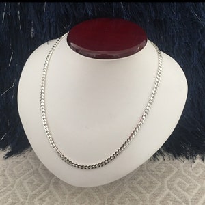 May include: A silver curb chain necklace on a white display stand. The chain is made of interlocking links.