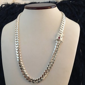 May include: A silver curb chain necklace with a red stone clasp.