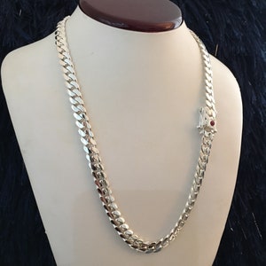 Può includere: Una collana a catena curb in argento con una chiusura in pietra rossa.
