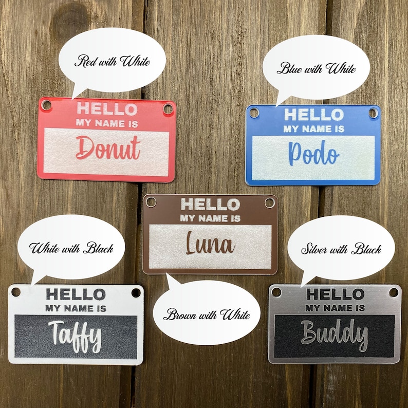 May include: Six different dog name tags with various colors and text. The tags are made of metal and have a hole for a leash. The text on the tags reads "HELLO MY NAME IS" followed by the dog's name. The names are Donut, Podo, Luna, Taffy, and Buddy. The colors of the tags are red, blue, brown, black, and silver.