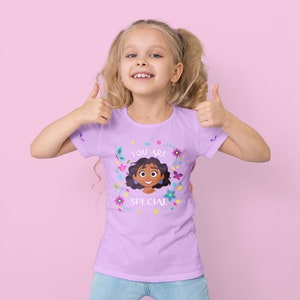 Puede incluir: Una ni&ntilde;a con cabello rubio lleva una camiseta morada con un dise&ntilde;o floral colorido y el texto "You are special". Est&aacute; haciendo un pulgar hacia arriba con ambas manos.