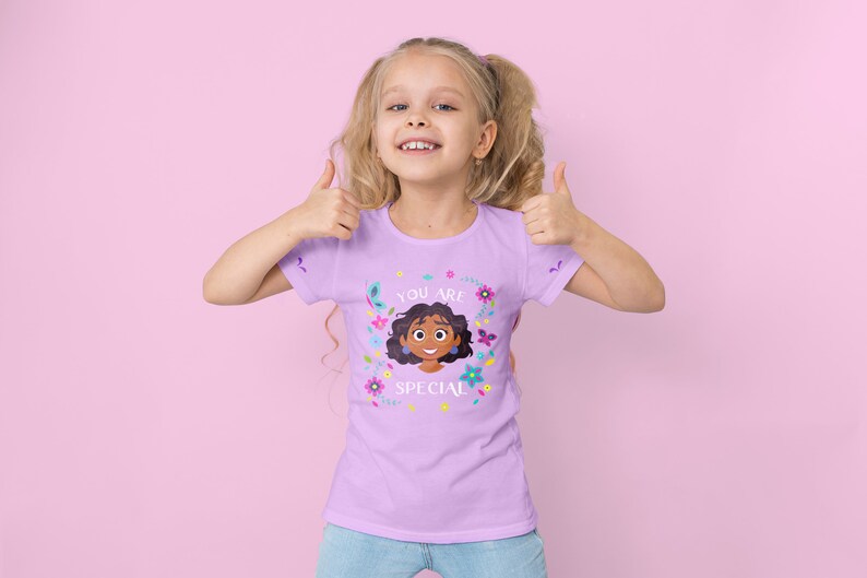 Puede incluir: Una ni&ntilde;a con cabello rubio lleva una camiseta morada con un dise&ntilde;o floral colorido y el texto "You are special". Est&aacute; haciendo un pulgar hacia arriba con ambas manos.