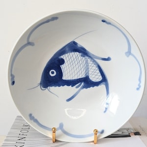 May include: A white ceramic bowl with a blue and white fish design. The bowl is on a gold stand.