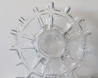 May include: Clear glass decorative bowl with a starburst design. The bowl has a central circular indentation and is placed on top of a book titled "The Kinfolk Home".
