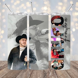 May include: A stainless steel tumbler with a black and white photo of a man wearing a cowboy hat and a black jacket. The tumbler has the word "Grupo" written in large letters on the side, with the word "Frontera" written in smaller letters below it.