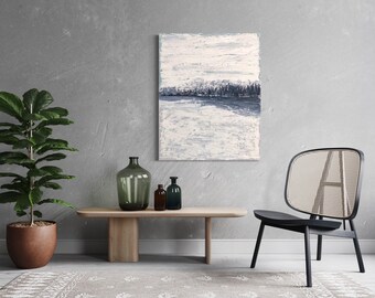 Op de afbeelding: Een lichtgrijze muur met een schilderij van een blauw en wit landschap, een plant in een pot, een houten tafel met drie glazen flessen en een zwarte stoel met een gevlochten rugleuning.