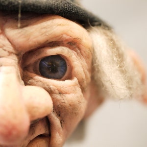 Könnte beinhalten: Nahaufnahme eines skurrilen Charakters mit einer großen, bauchigen Nase, einem blauen Auge und einem weißen, flauschigen Bart.