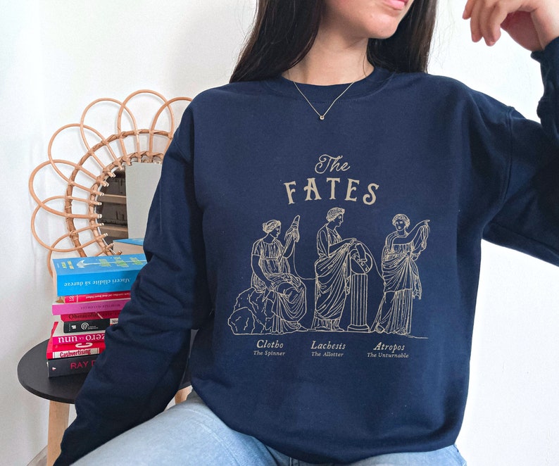 May include: A navy blue sweatshirt with a graphic of three women representing the Greek Fates, Clotho, Lachesis, and Atropos. The text "The Fates" is printed above the graphic.