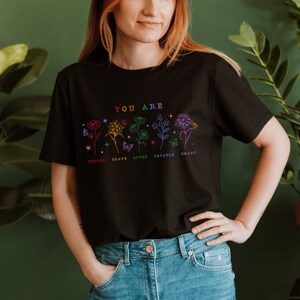 May include: Black t-shirt with a floral design and the text "YOU ARE" above the words "STRONG, BRAVE, LOVED, CAPABLE, SMART".
