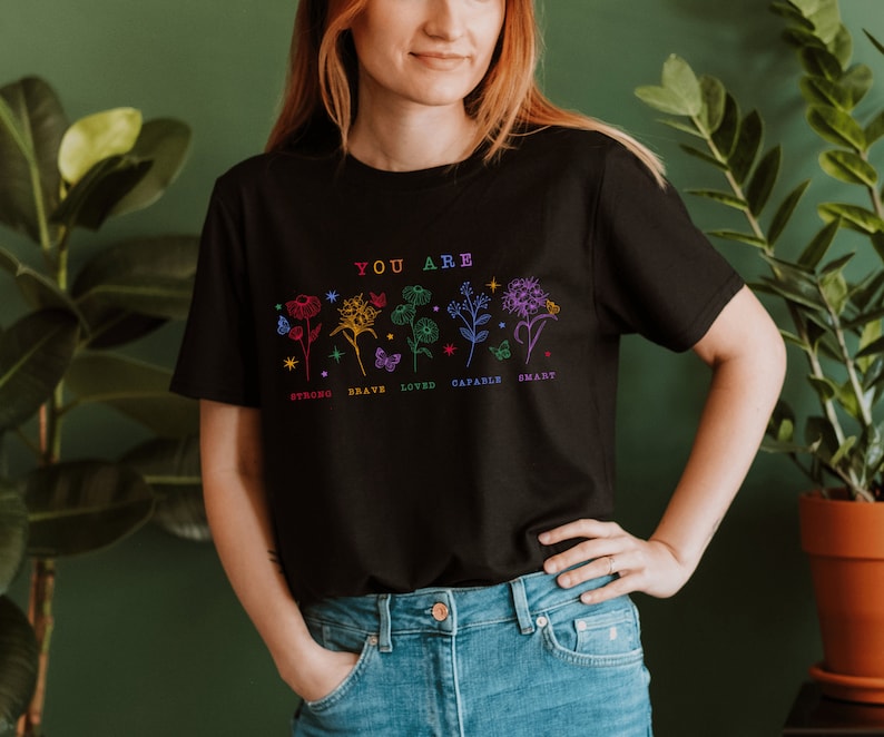 May include: Black t-shirt with a floral design and the text "YOU ARE" above the words "STRONG, BRAVE, LOVED, CAPABLE, SMART".