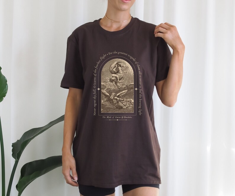 May include: A brown t-shirt with a vintage illustration of a winged figure falling from the sky. The text on the shirt reads "Never regret the fall, O learners of the fearless flight. For the greatest tragedy of all time is never to feel the burning light. The Myth of Icarus & Daedalus."