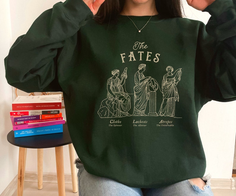 May include: A dark green sweatshirt with a graphic print of three figures representing the Fates, Clotho, Lachesis, and Atropos. The text "The Fates" is printed above the figures.